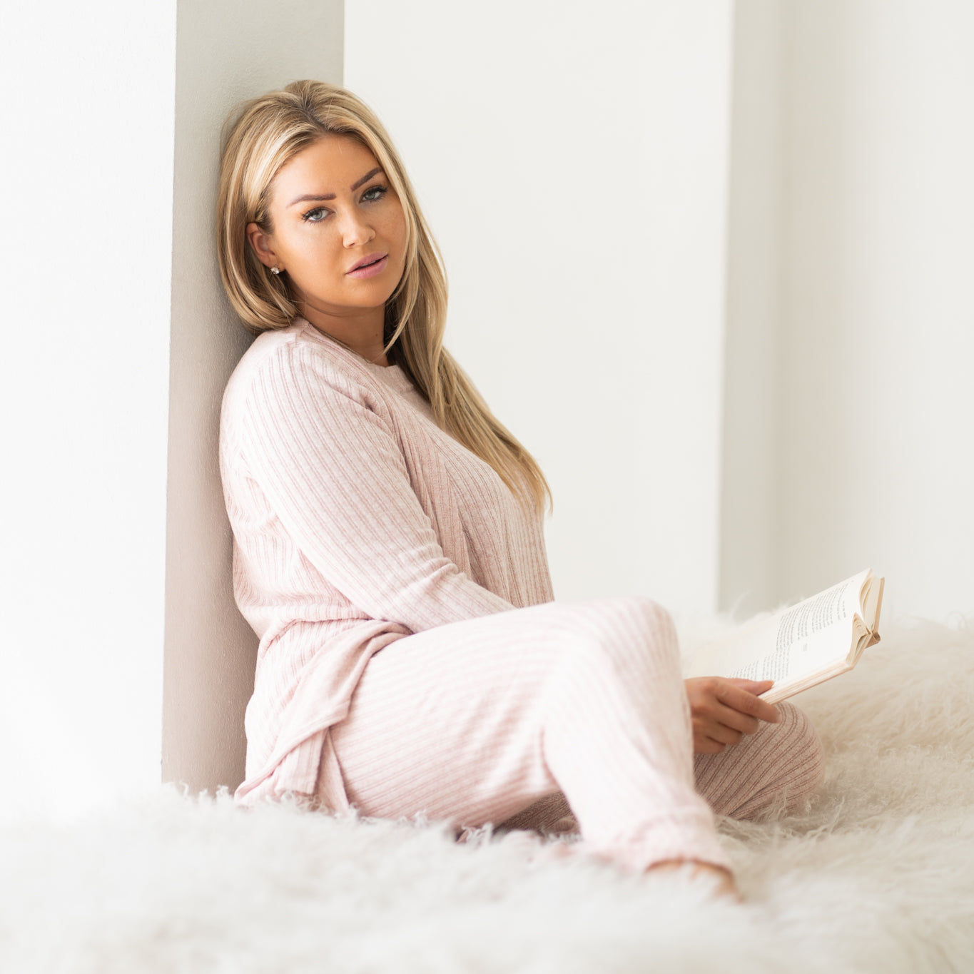 Woman staring at camera sitting on cozy white bed wearing pink cozy three piece lounge set, Shop T.K.S