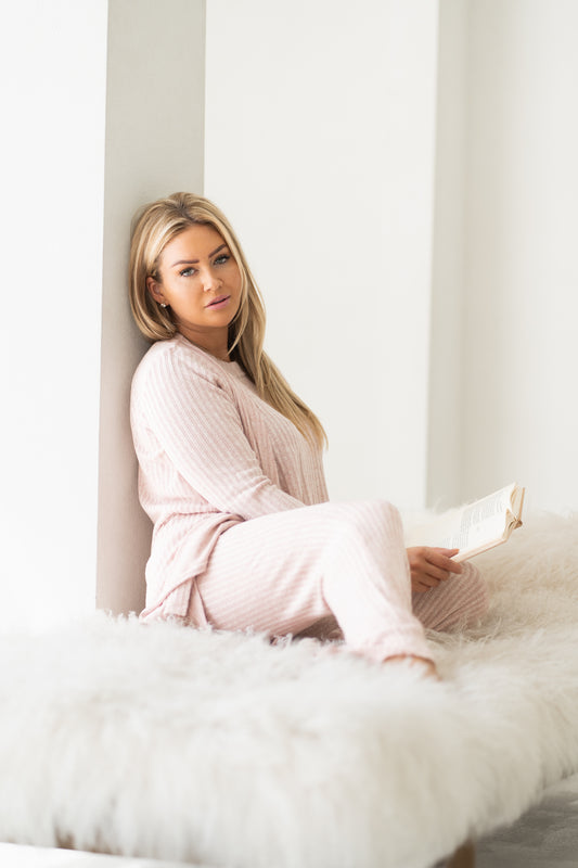 Woman staring at camera sitting on cozy white bed wearing pink cozy three piece lounge set, Shop T.K.S