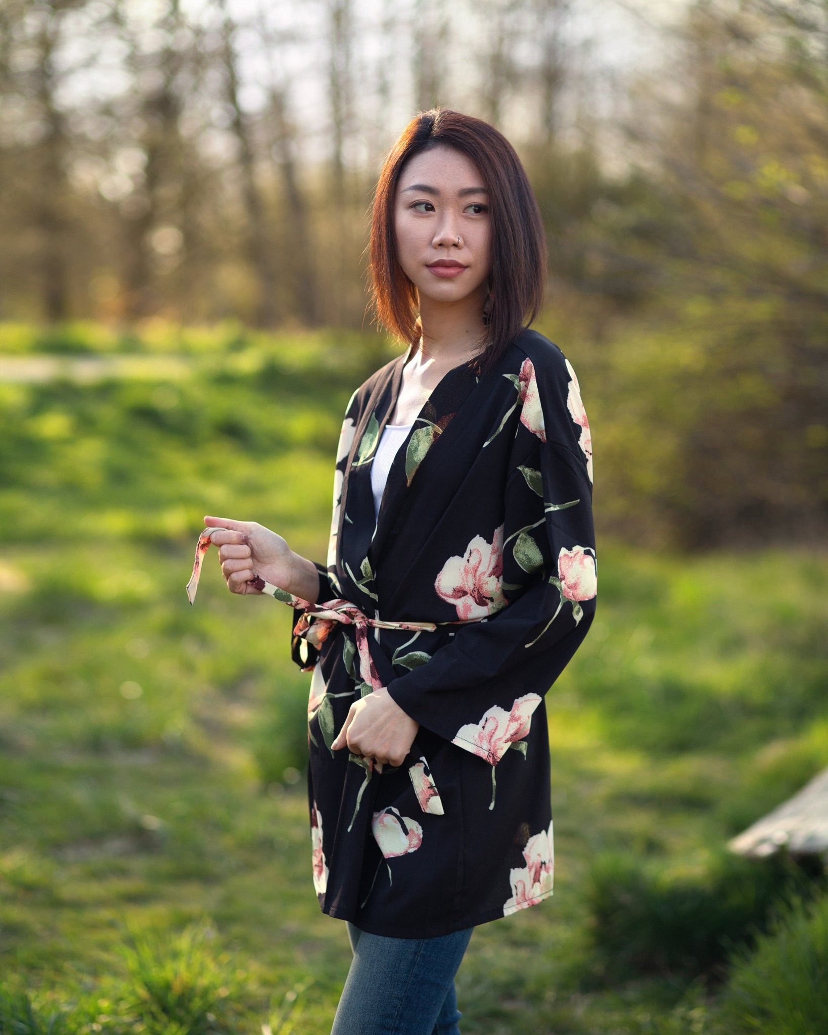 Woman wearing black and floral blazer robe standing in green forest, Shop T.K.S