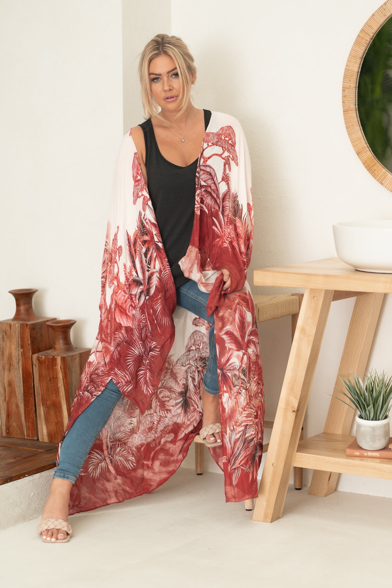 woman sitting wearing white and red floral beach cover up with jeans and black tank top