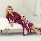 Woman wearing floral burgundy robe sitting on white couch, birthing robe, maternity clothing