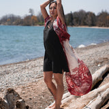 woman standing on log with hands up wearing long flowy white beach over up and black dress