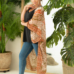 Woman wearing boho orange and cream print beach cover up, Shop T.K.S, front with hand