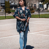 Woman wearing navy blue floral short beach cover up and bamboo tank top with jeans, staring away from camera Shop TKS