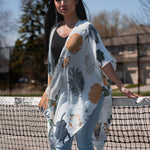 Woman wearing white floral beach cover up standing in front of tennis court net, with jeans and bamboo tank top, Shop T.K.S