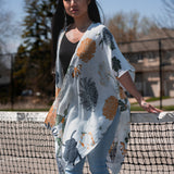 Woman wearing white floral beach cover up standing in front of tennis court net, with jeans and bamboo tank top, Shop T.K.S