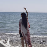 video of woman wearing long white beach floral cover up and standing on log