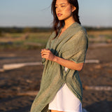 Woman staring into distance wearing green beach cover up and white dress smiling