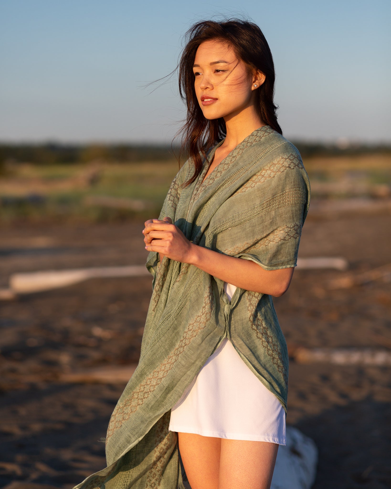 Woman staring into distance wearing green beach cover up and white dress smiling