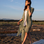 Women standing on beach wearing green beach cover up staring at sunset