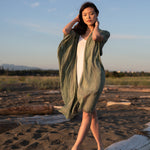Woman staring at camera wearing green beach cover up standing on white log