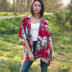 Woman wearing coral and floral short beach cover up for vacation standing in forest, Shop T.K.S
