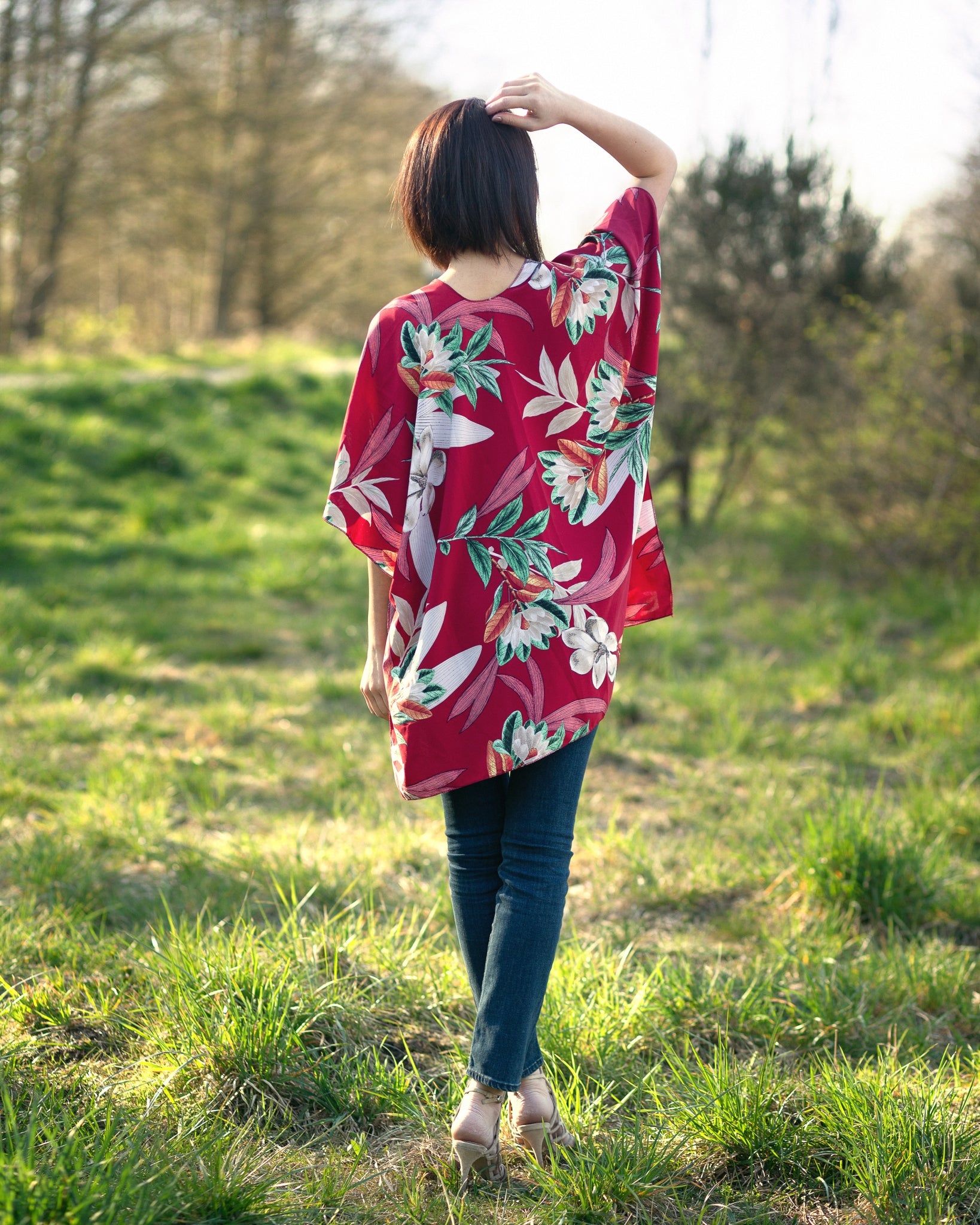 Woman wearing coral and floral short beach cover up for vacation standing in forest facing back, Shop T.K.S