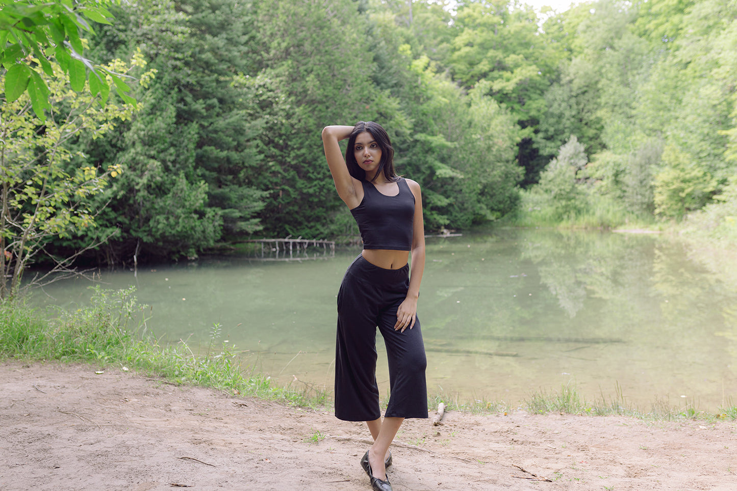 Woman standing with hand behind her head wearing black bamboo crop top and wide legged lounge pants, Shop T.K.S