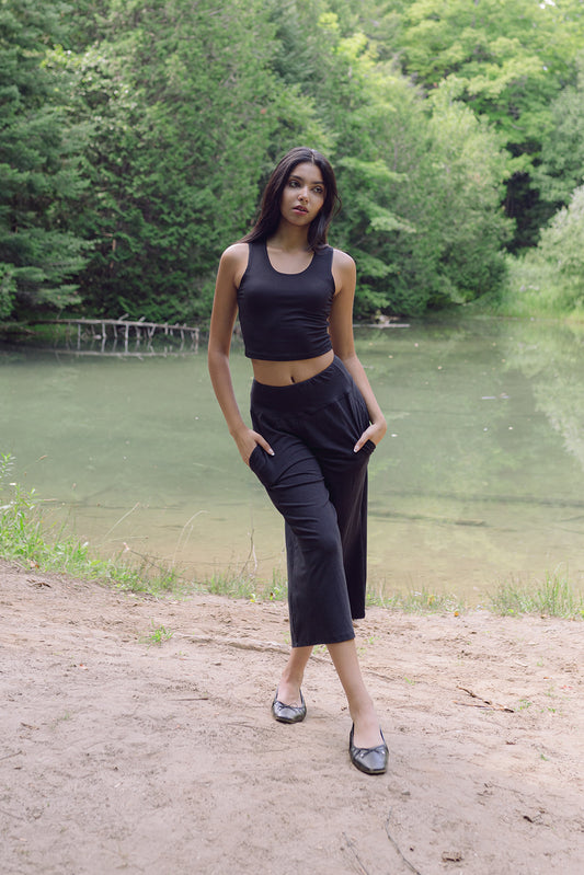Woman wearing black wide lounge pants with hands in pockets standing in front of pond