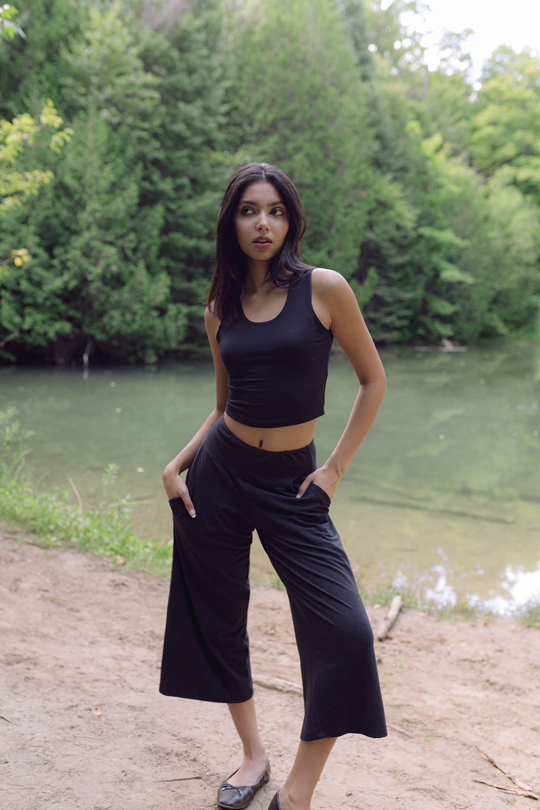 Woman wearing black wide legged lounge pants with hands in pockets and black bamboo crop top , Shop T.K.S