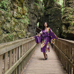 Women standing in between two rocks wearing long floral robe iwth kimono robes and floral and butterfly design, standing on bridge wearing black ballet flats