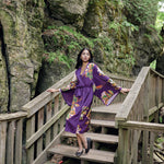 Woman looking over shoulder standing on bridge wearing long purple robe with kimono sleeves and butterfly and floral print design