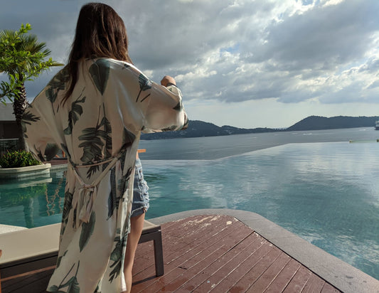 Women staring at ocean with palm tree in background wearing short white and palm leaf print palma robe, Shop T.K.S