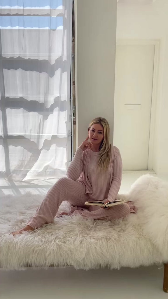 video of woman in pink lounge set reading beside window