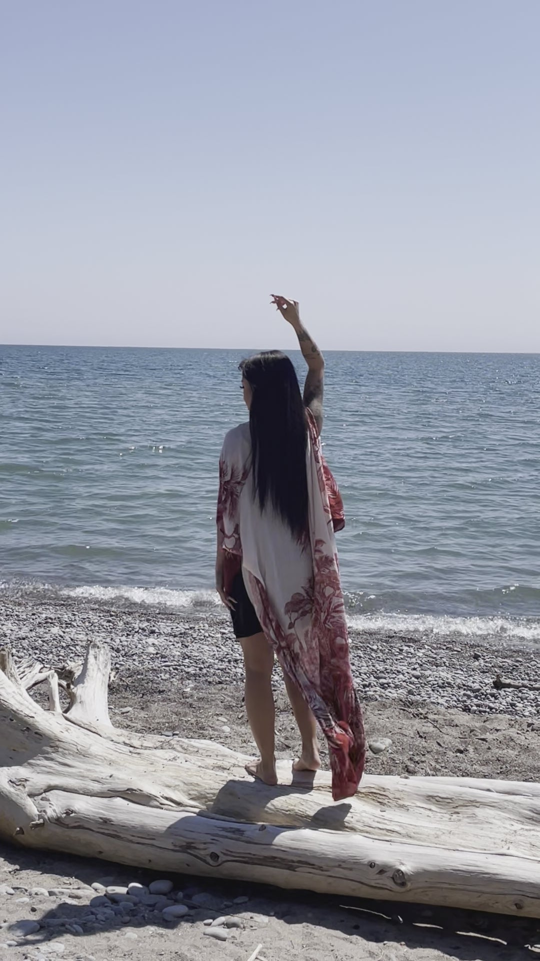 video of woman wearing long white beach floral cover up and standing on log