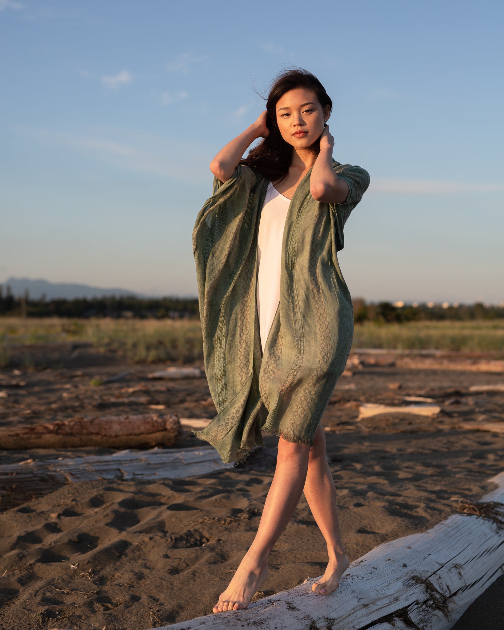 Woman staring at camera wearing green beach cover up standing on white log