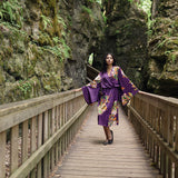 Women standing in between two rocks wearing long floral robe iwth kimono robes and floral and butterfly design, standing on bridge wearing black ballet flats
